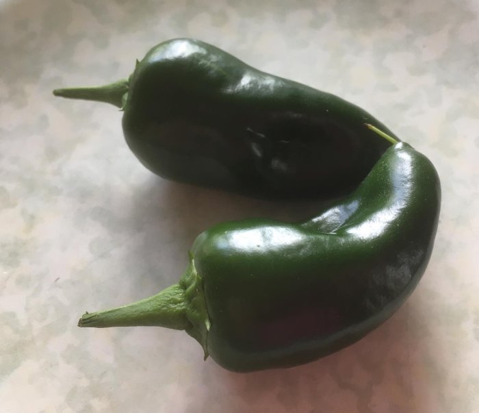 Två gröna padrone-paprikor på ett köksbord.