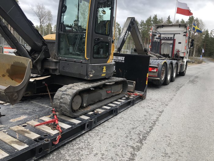 Grävmaskin på lastbilsflak redo för transport vid uppfräschning av gård.