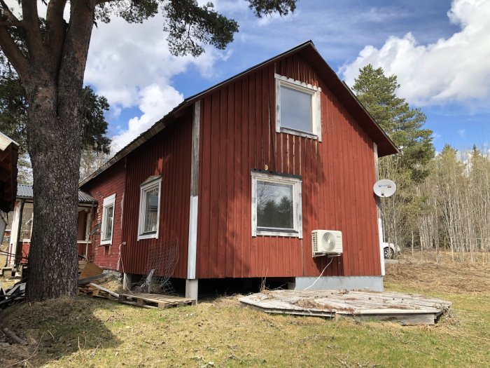 Rödmålat hus med vita fönsterkarmar och parabolantenn under en solig himmel.