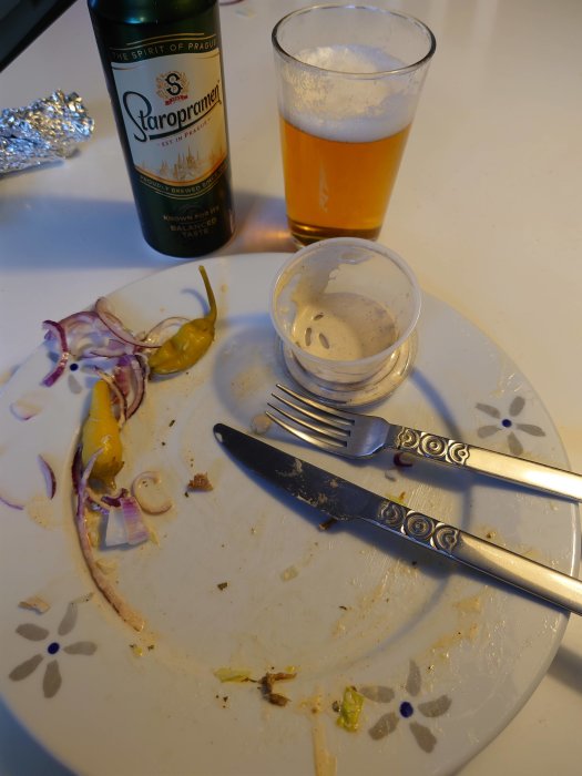 Efter måltid scen med halvtomat ölglas, Staropramen-flaska och en smutsig tallrik med matrester och bestick.