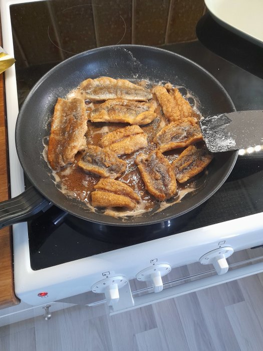 Stekt sill i en stekpanna på spisen redo för att läggas in med lök och ättika.