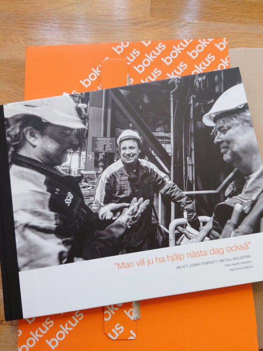 Två arbetare i en industrimiljö delar ett leende, en bär hjälm, nära texten "Man vill ju ha hjälp nästa dag också".