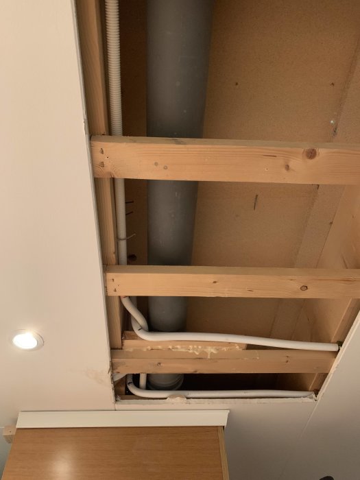 Öppen taksektion som visar träbjälkar, rörledningar och isolering i ett pågående bygg- eller renoveringsprojekt.