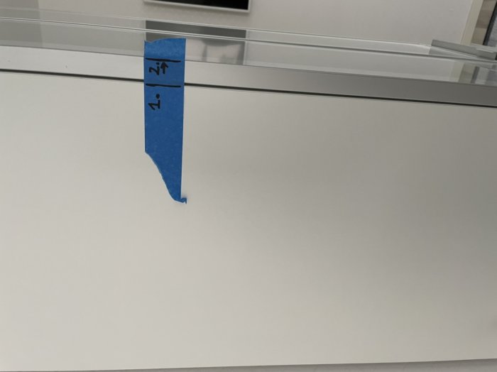 Vit köksinredning med silverkant på en dörr och blå maskeringstejp.