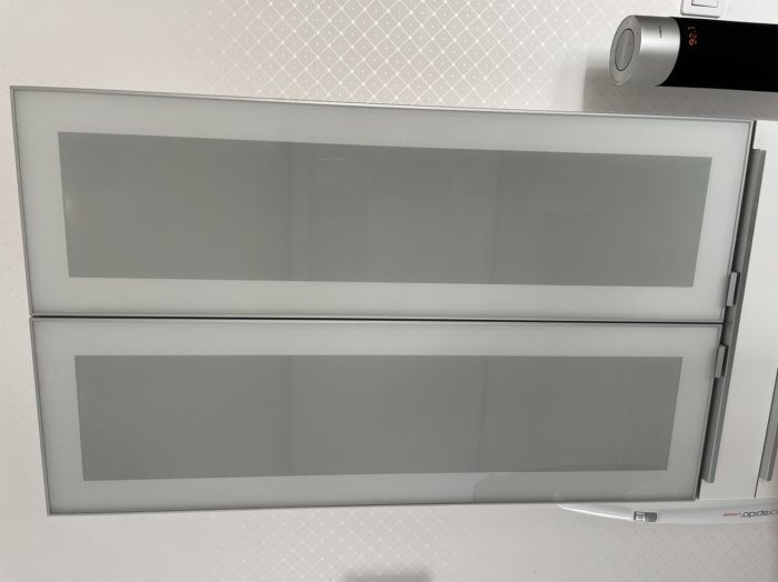 Grå köksskåp med frostat glas och silverkant monterat över vit bänkskiva.