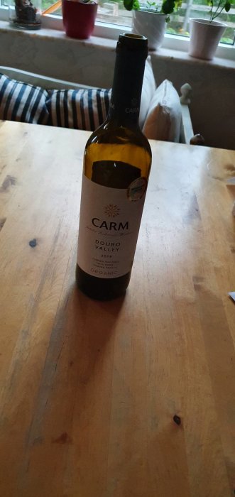 Flaska rött vin CARM Douro Valley 2019 på träbord, skämtsamt betecknat som 'karma'.