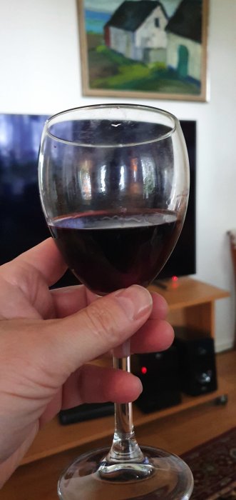 Ett glas rött vin i förgrunden med ett oljemålning av ett hus i bakgrunden.