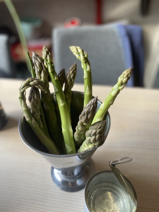 Färsk sparris i en stålkanna på ett köksbord, bredvid en öppen glasburk.