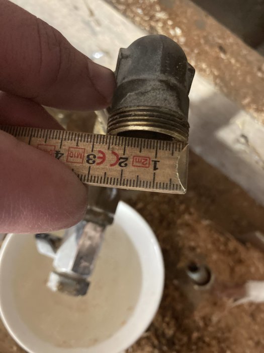 Hand håller ett måttband mot ett rör för att mäta dess diameter, röret synes ha metriska mått runt 20 mm.