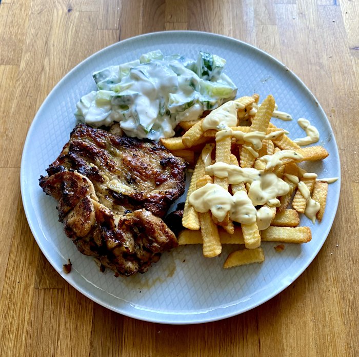 Grillat urbenat kycklinglår med pommes och tzatziki på en tallrik.