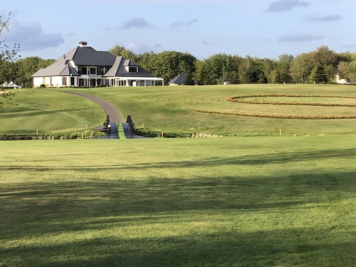 Hus med veranda och takfönster omgivet av välskött gräsmatta med slingrande väg och häckar.