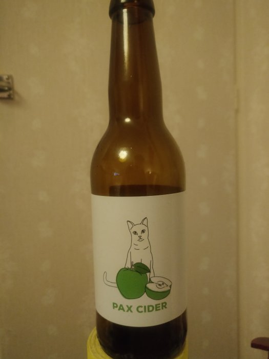 Flaska med etikett "PAX CIDER" och illustration av en katt med äpplen.