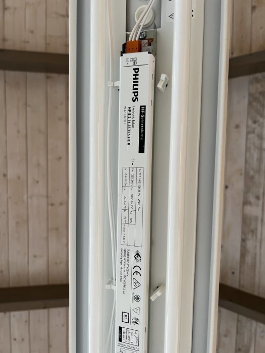 Öppen lysrörsarmatur monterad i tak med synlig Philips drivdon och två lysrör.