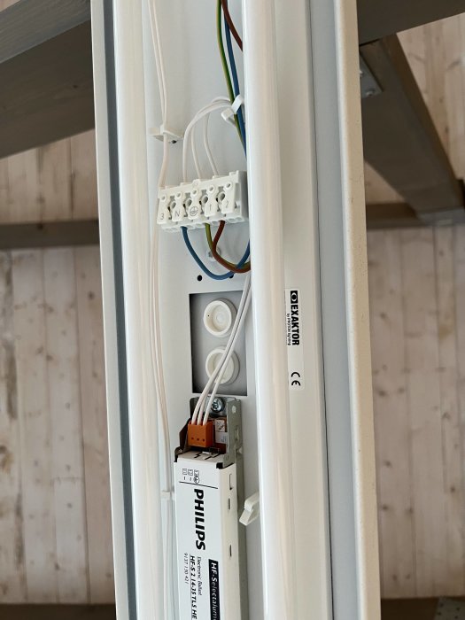 Öppen lysrörsarmatur i carport med synlig ballast och kopplingsdosa för felsökning, kablar är kopplade men ingen lampa är tänd.
