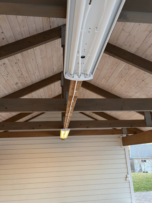 Lysrörsarmatur i träkonstruerad carport med ett tänd lysrör och en avstängd.