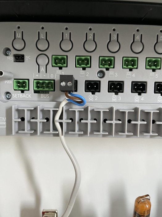Ställdon och trådlös termostat med oanslutna blå och bruna kablar framför en svart elplint.