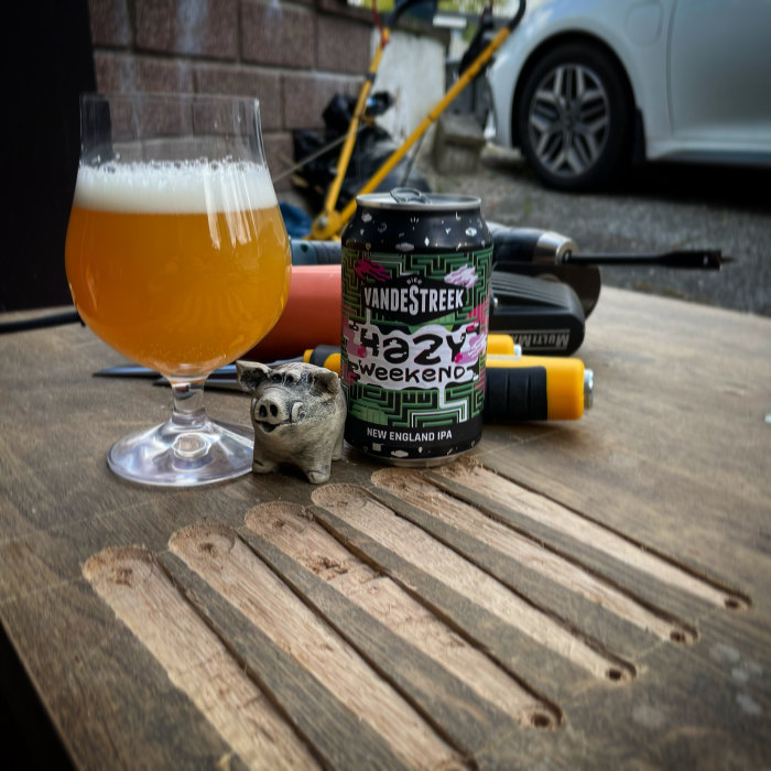 Ölglas med skummad dryck och burk på träyta med suddig bakgrund av verktyg och cykel.