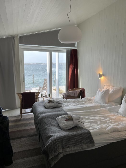 Hotelrum med säng, hängande lampa och fönster med utsikt över havet.