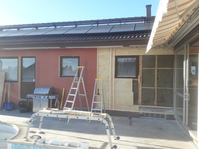 Renovering av fasad med isolering och fönsterbyte, delvis omputsad vägg och arbetsmaterial med stege.