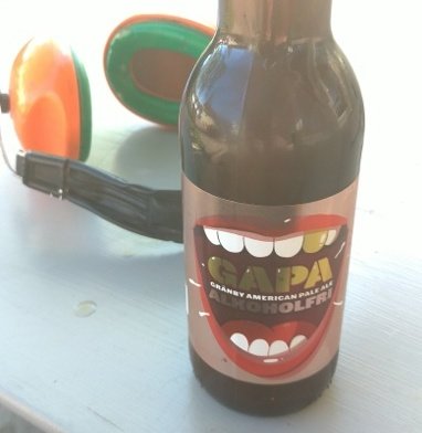 Flaska med GAPA amerikansk pale ale bredvid ett par solglasögon på ett bord utomhus.