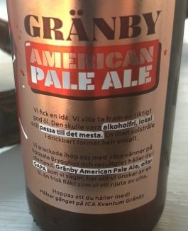 Ölflaska med etikett för 'Gränby American Pale Ale' på ett bord.