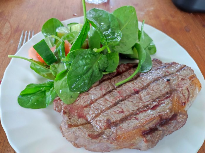 Grillad biff med sallad av spenat, tomat och gurka på en vit tallrik.