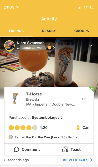 Ölglas med grumlig, gul vätska och ölburk med hästsjuhuvuddesign bredvid lergris på bord.