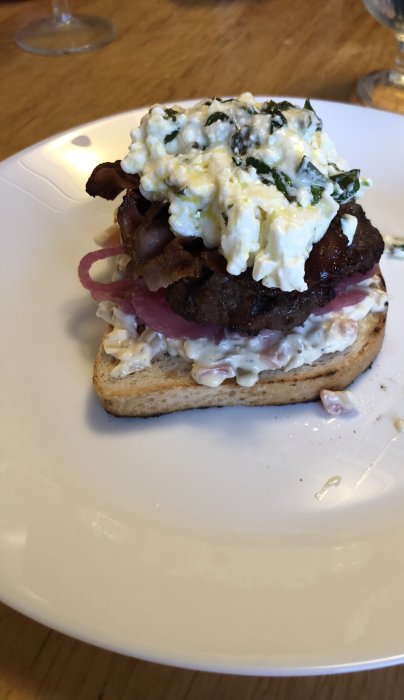 Hamburgare med fetaoströra, picklad rödlök och bacon på en halv brödbit.