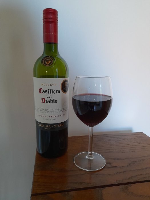 Flaska av Casillero del Diablo vin och ett fyllt glas på ett träbord mot ljus bakgrund.