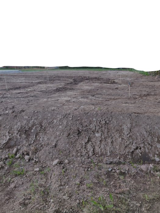 Uppschaktad tomt med ojämn mark och stenar, potentiell placering för friggebod.