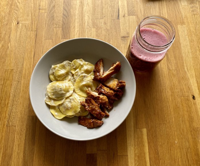 Ravioli och grillad kycklingfilé på tallrik med ett glas mousserande blåbärsvin på träbord.