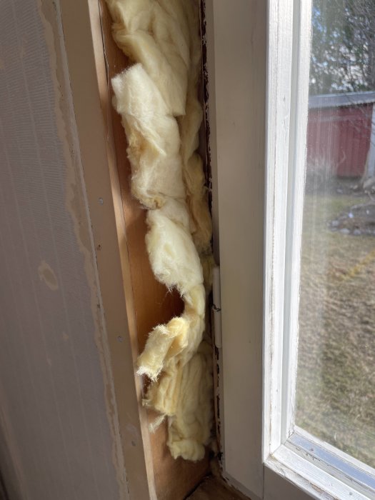 Isoleringsmaterial som ligger löst intill en träregel under ett fönster, inga synliga fuktskador.
