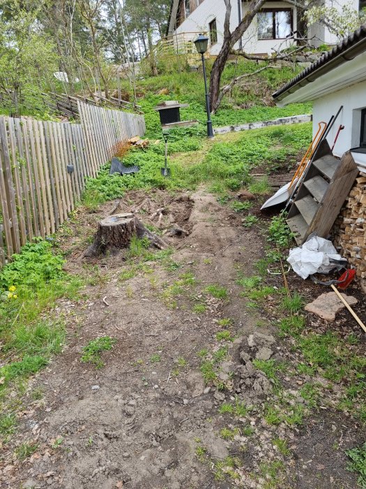 Ojämn trädgårdsmark med stor stubbe och rötter, planering för parkering nära spade och stödmur.