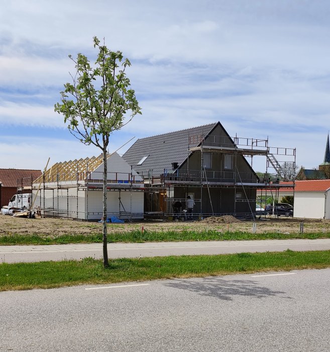 Ett hus under byggnad med blottade gråa väggar och uppförda takstolar.