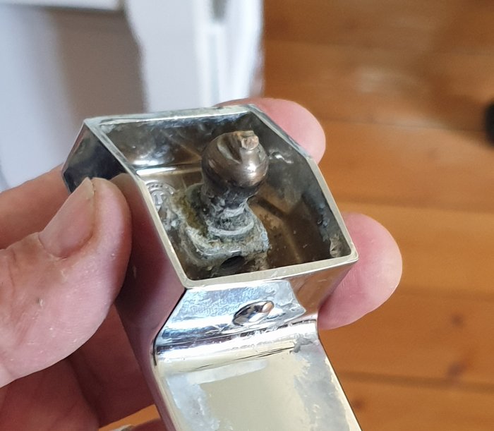 En person håller ett dörrhandtag med en urskruvad insexskruv och synliga skador, mot bakgrund av trägolv.