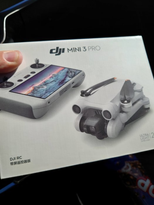 Hand håller förpackning för DJI Mini 3 Pro drönare med kontroll och drönare avbildade.