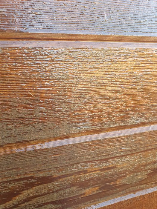 Blöt cederträpanel med flagnande oljefinish, visar åldring och underhållsbehov.