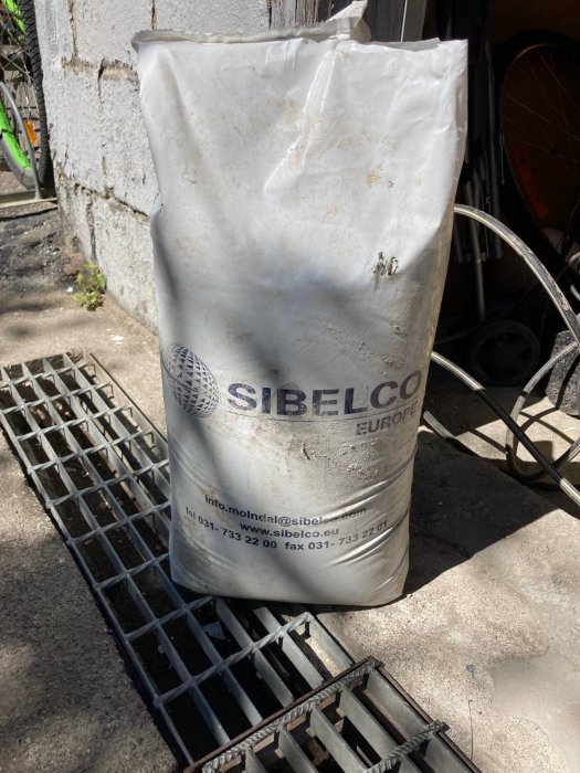 En säck märkt med "SIBELCO" står i ett garage, innehållet syns ej.