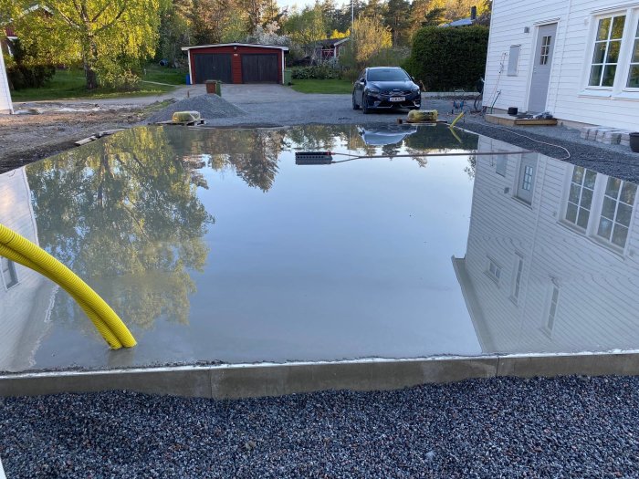 Nyutgjuten betongplatta för garage med reflekterande yta och kantskoningsjärn synligt.