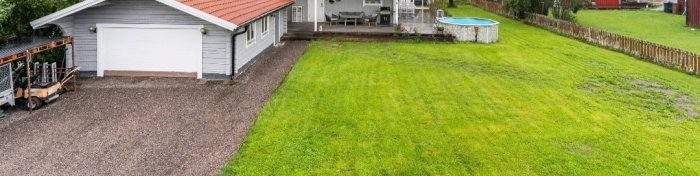 Hus med tillbyggnad och garage intill grön gräsmatta med pool och altan.