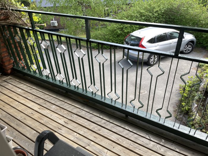 Renoverad balkong med nymålad grön räcke, rostbehandlad, med latexfog och trägolv, utsikt över parkerad bil.