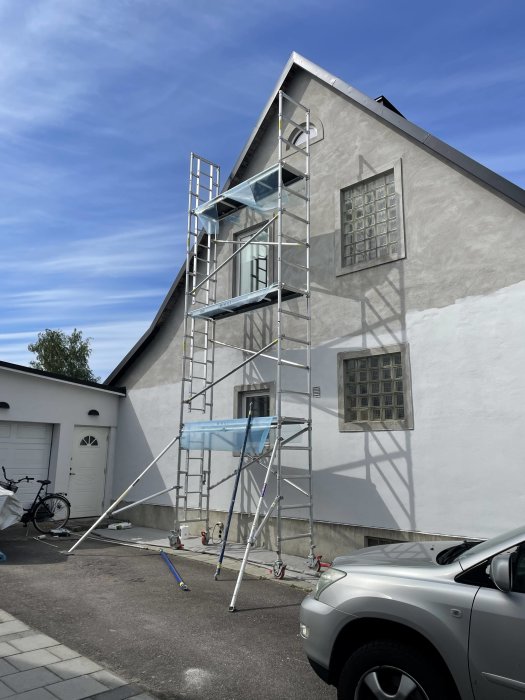 Byggställning monterad vid sidan av ett hus för målningsarbete under en klarblå himmel.