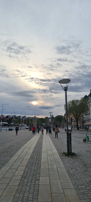 Solnedgång över Strandvägen i Stockholm med promenerande människor och stadsliv.