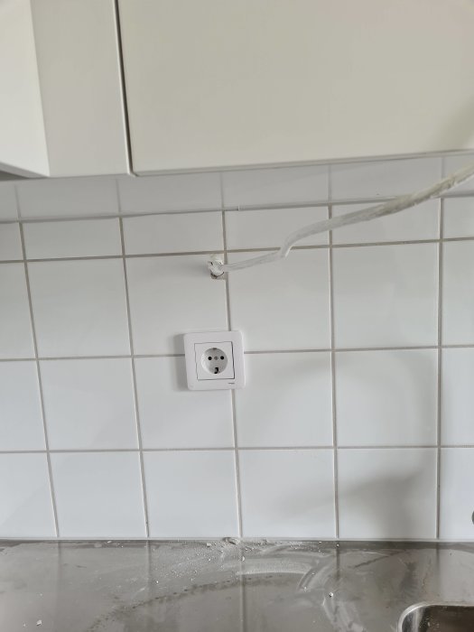 Eluttag på kakelvägg över diskbänk med kabel dragen till ett skåp ovanför.