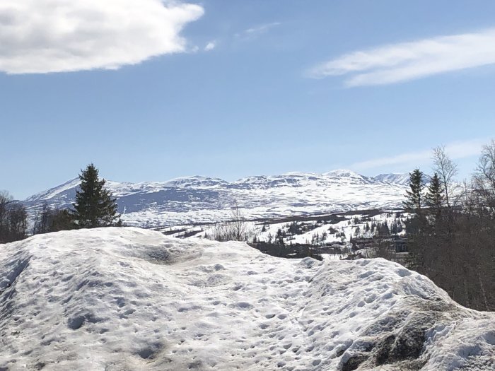 Snötäckt landskap med berg under en klarblå himmel, snö smälter i solskenet.