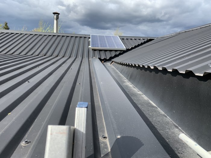 Tak av plåt med solpanel och en skorsten i bakgrunden, möjlig indikation på dålig tätning som kan orsaka fukt.