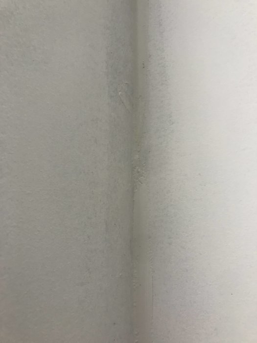 Ojämn fog på vitmålad vägg med dålig finish och fläckar av spackel.