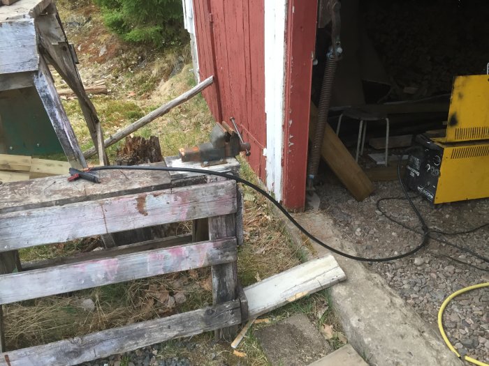Gammal gul svetsmaskin Decamig 318 vid en röd byggnad med kablar och verktyg på marken.