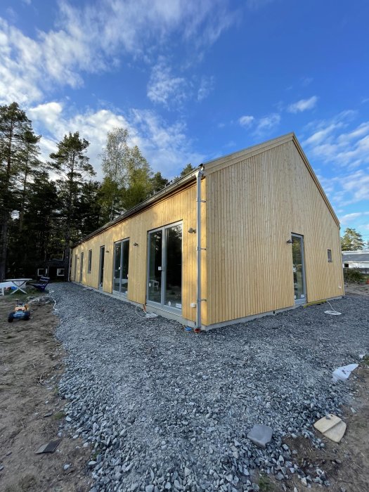 Nybyggt trähus med omgivande makadam och byggmaterial på marken.