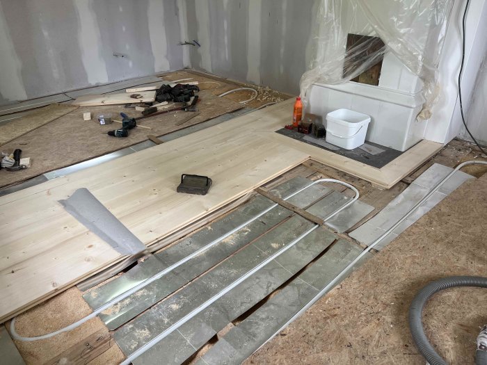 Påbörjad installation av trägolv med verktyg och skruvar, i ett rum under renovering.
